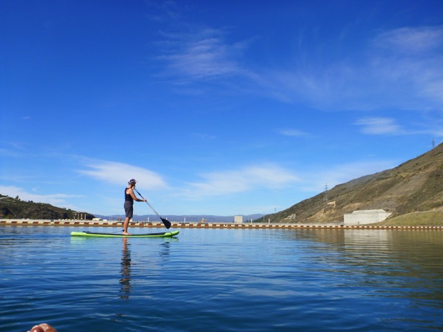 Jude paddles past with the view of the top of Clyde Dam sits on the other side of her.